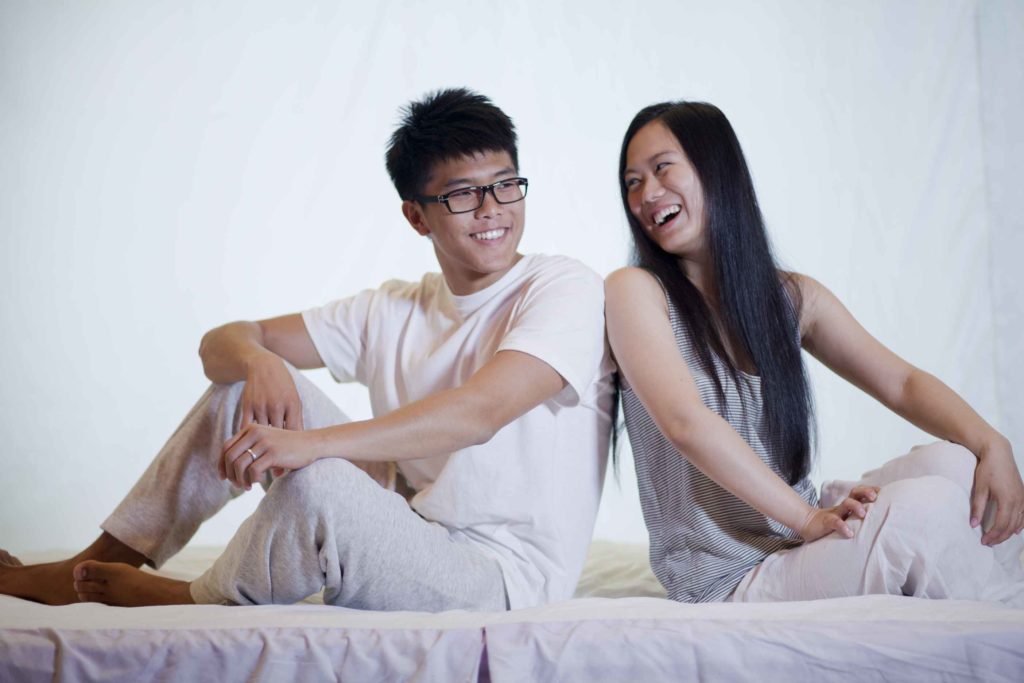 A couple sitting on a bed. Most healthy adults need between 7 to 9 hours of sleep per night to function optimally.