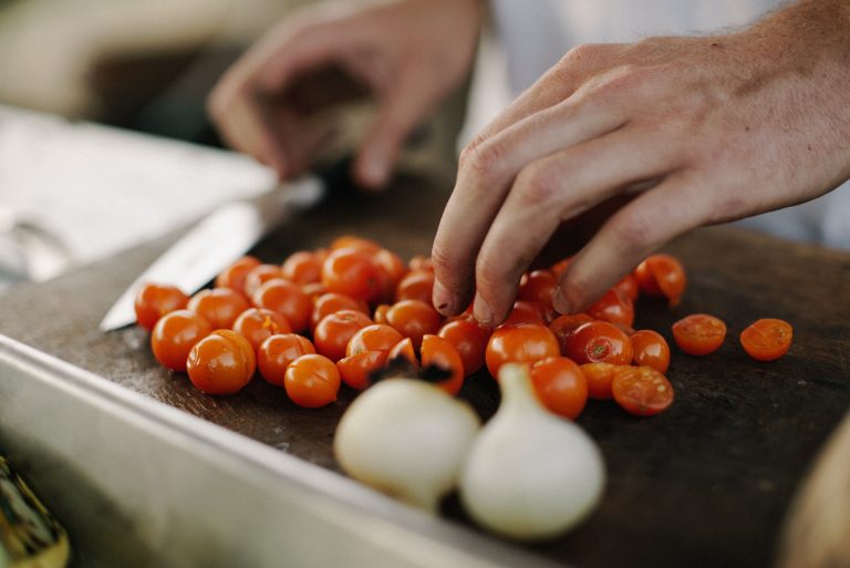 Cutting board with cherry tomatoes and pearl onions. The absorption of lycopene from tomatoes is enhanced when cooked with diced onions.