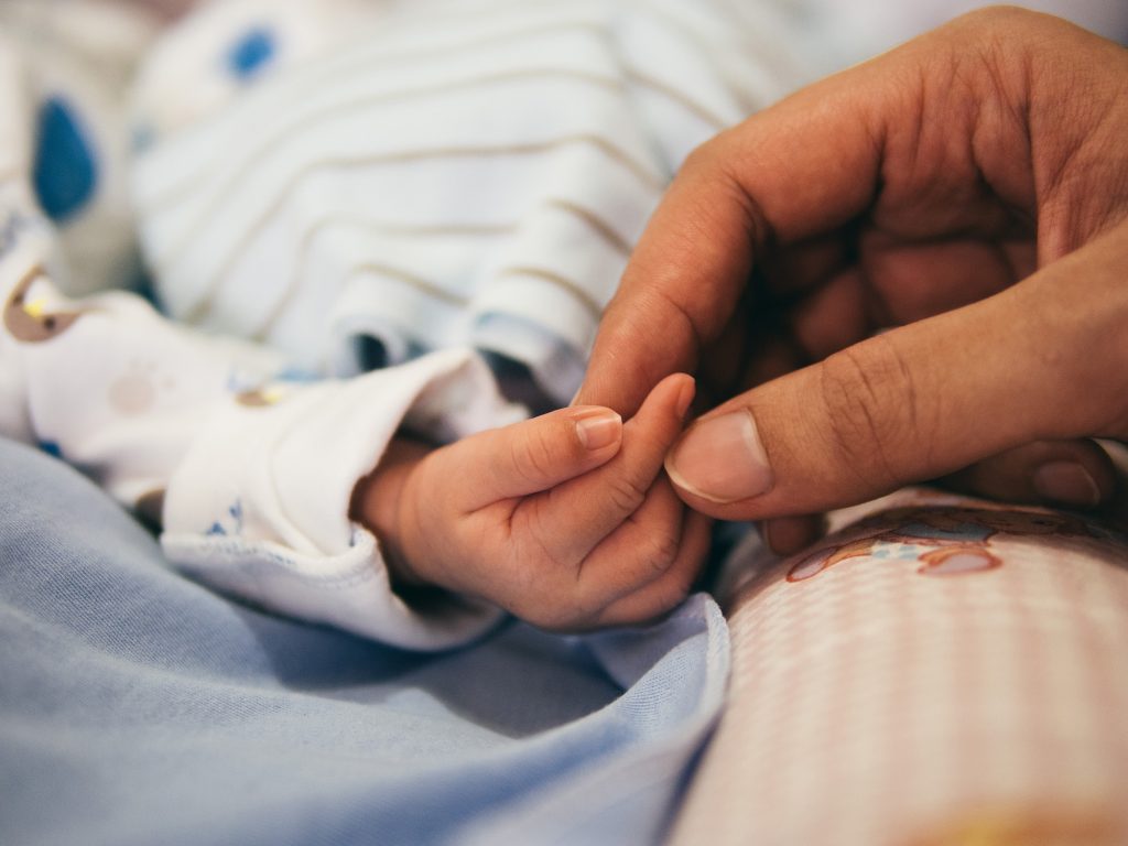 An adult gently holds the fingers of a newborn. Most rare diseases affect children.