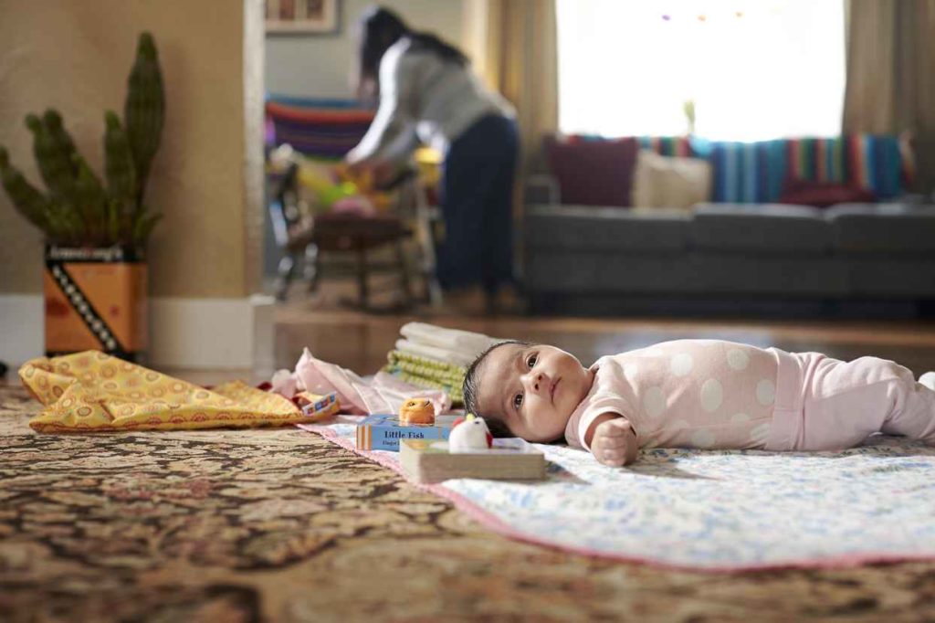 Baby who may live beyond 100 years laying on a blanket with mother in the background.