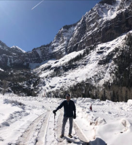 Healthy older man standing on a snowy road with mountains in the background.
