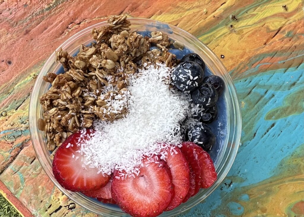 A bowl of grains fruit and yogurt on a rainbow colored tabletop.